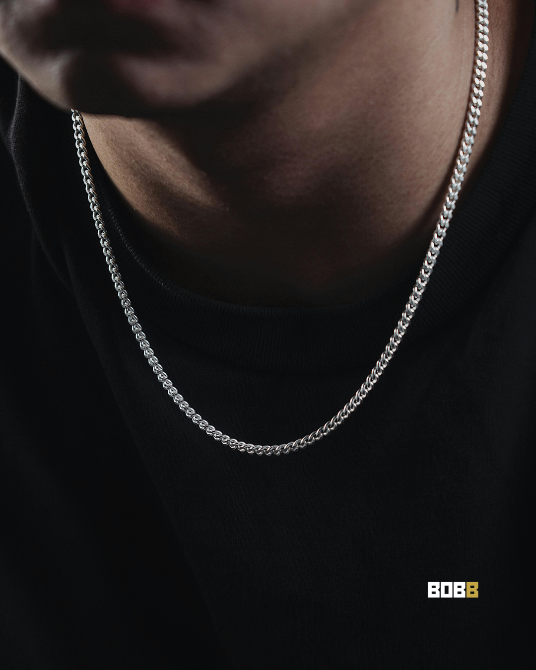 Close-up of a silver chain worn over a black t-shirt, photographed in warm low light